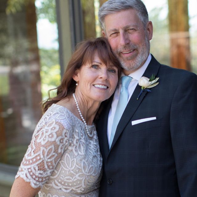 Bruce Robert Hough in a white shirt and black coat posing with his wife in a white floral net gown.